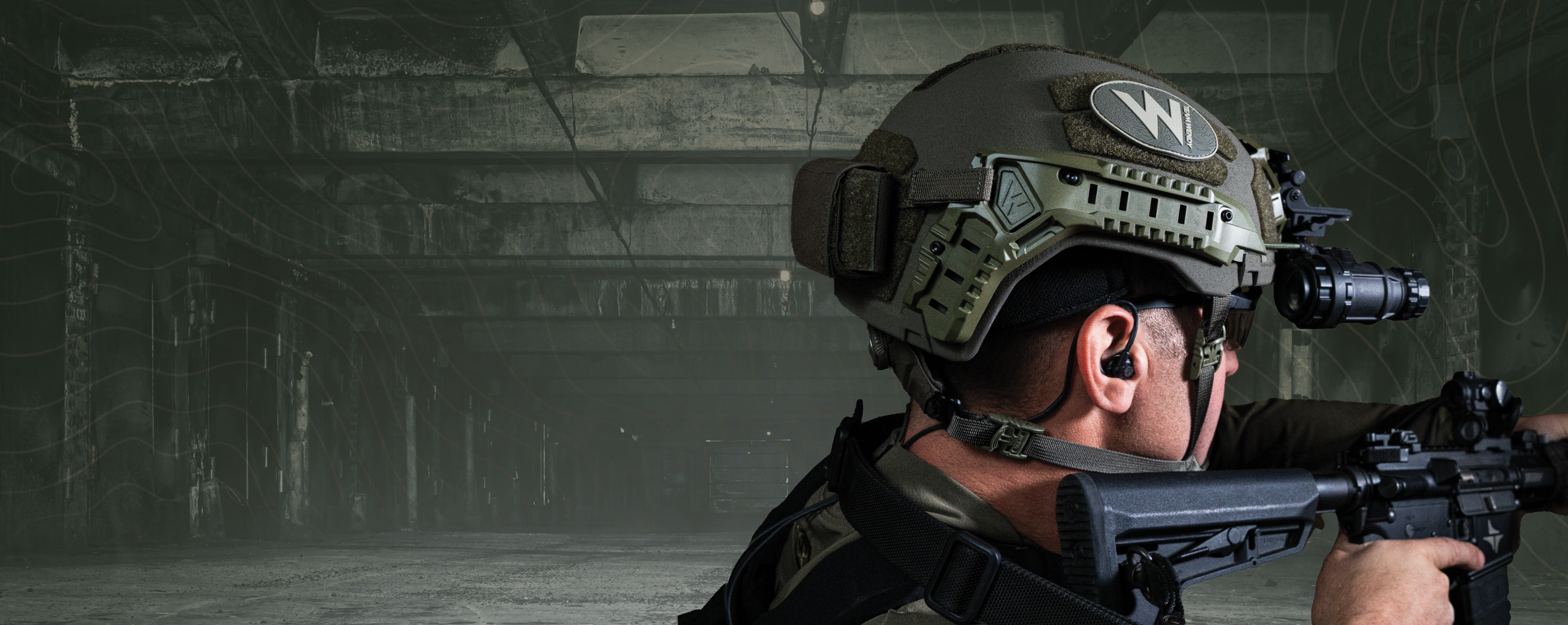 Person in tactical gear with a helmet and rifle in a dimly lit indoor setting